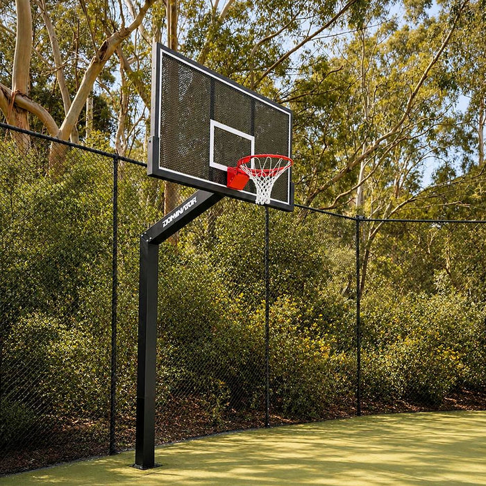 Dominator 72 inch fixed height basketball hoop with perforated aluminium backboard installed on a fenced sports court